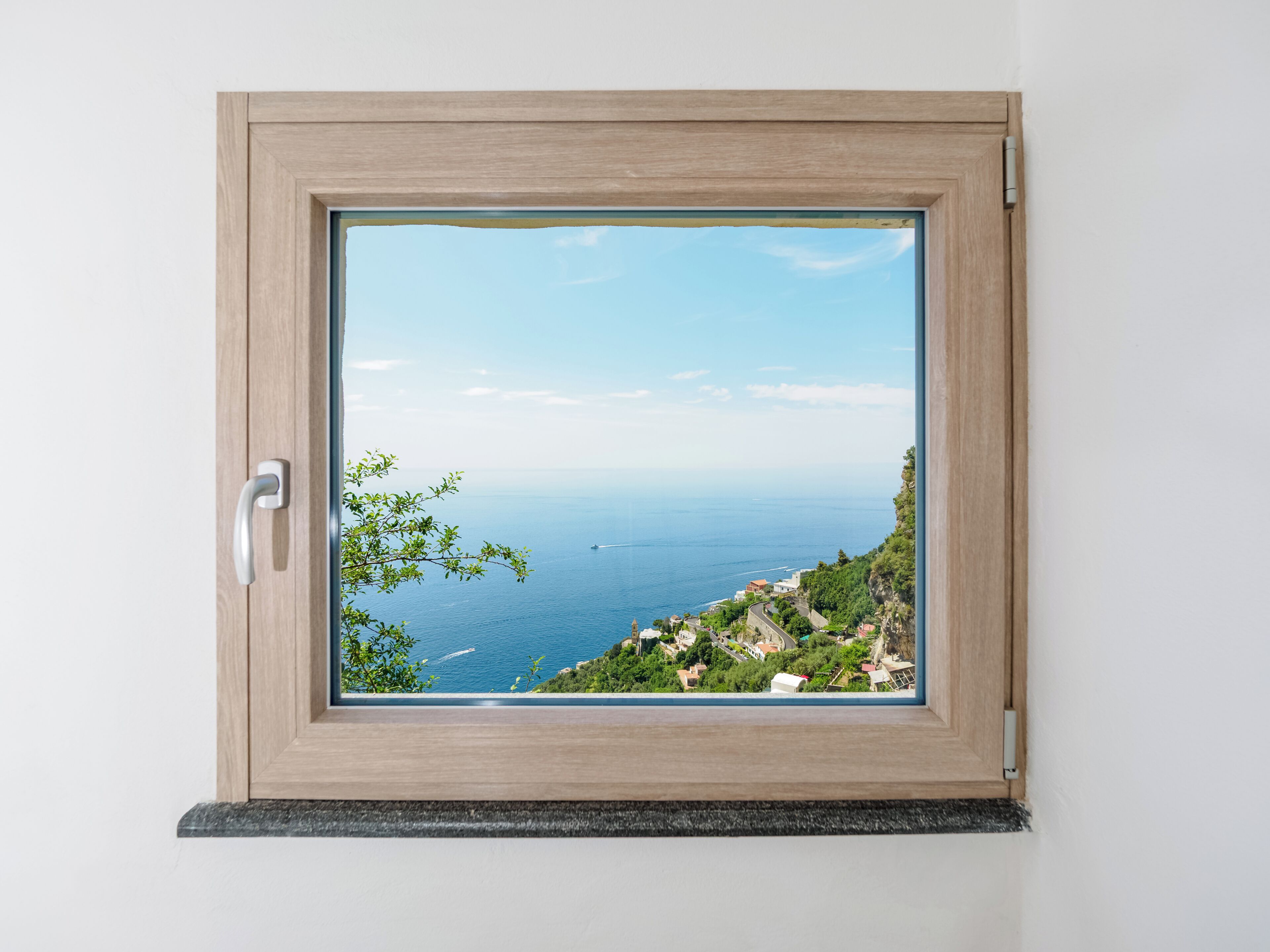 A window with a view of a coastal landscape, a door handle, and a wooden frame.