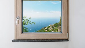 A window with a view of a coastal landscape, a door handle, and a wooden frame. - De Vivo Realty - Boscosfera Amalfi (Amalfi)