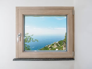 A window with a view of a coastal landscape, a door handle, and a wooden frame. - De Vivo Realty - Boscosfera Amalfi (Amalfi)