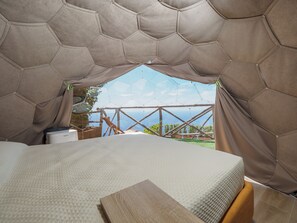 Une structure en forme de tente, avec un lit à l’intérieur, une vue sur l’extérieur et une table en bois.