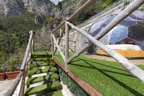 Eine Holztreppe mit Rasenanteppichstufen, einem Metallgeländer und Blick auf eine gebirgige Landschaft.