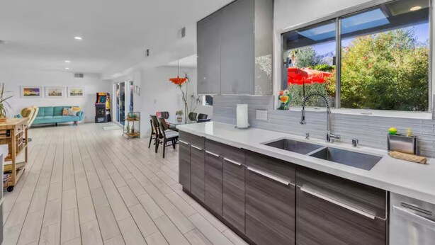 Een moderne keuken met een groot schiereiland, een zithoek met een blauwe bank, en uitzicht op groen.