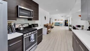 Een moderne keuken met een magnetron, fornuis en oven, een eethoek met een tafel en stoelen, en een woonkamer met een bank en televisie.
