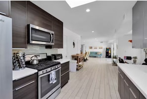 Eine moderne Küche mit Mikrowelle, Herd und Backofen, ein Essbereich mit Tisch und Stühlen sowie ein Wohnzimmer mit Sofa und Fernseher.