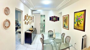 A dining area with a glass table, chairs, and a kitchen in the background. - Vacanze - Don Felipe (Maceió)