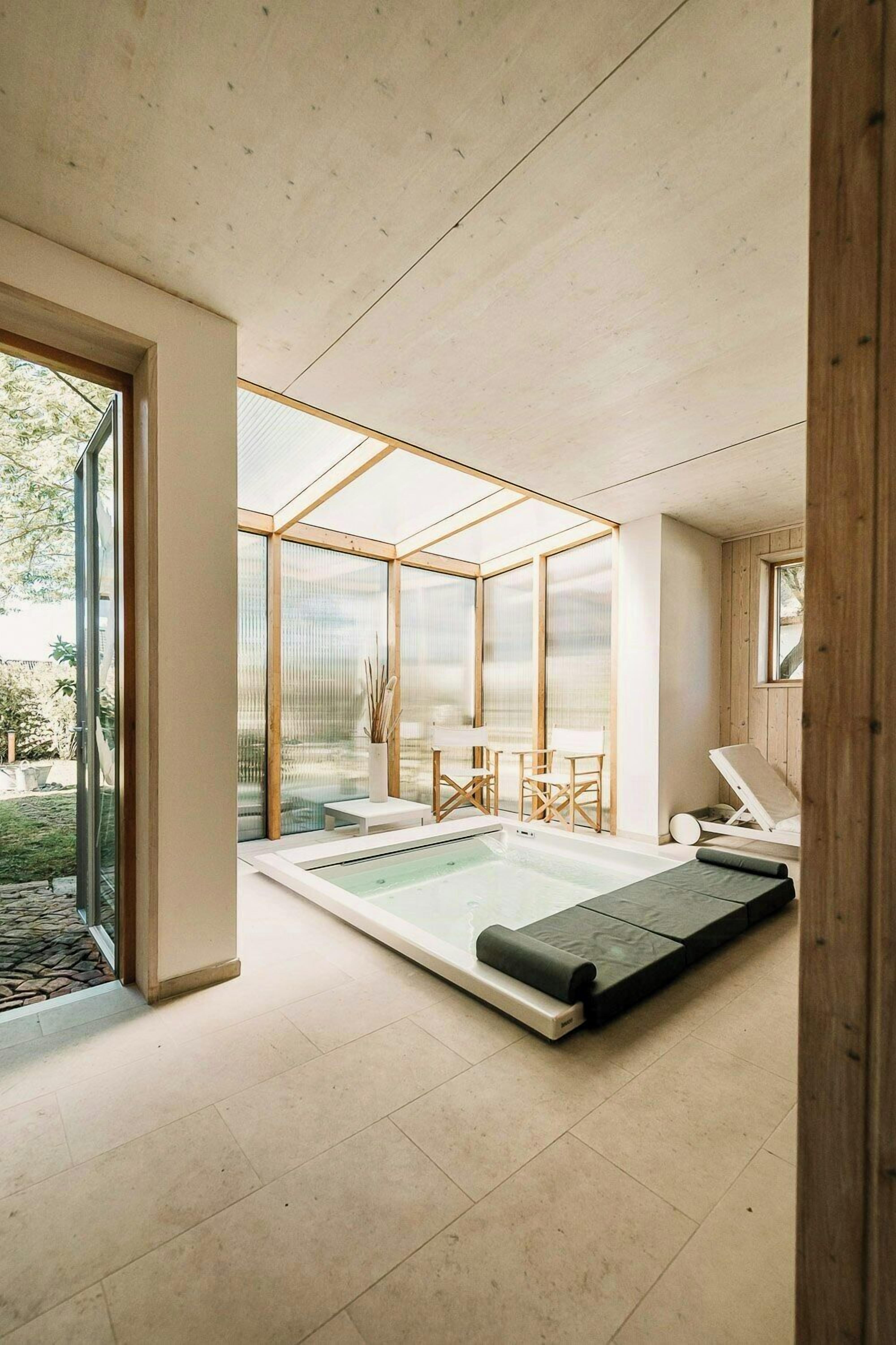Ein moderner Wellnessraum mit einem in Glas eingefassten Whirlpool, Holzmöbeln und Blick ins Freie.