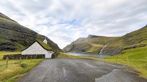 A rural church with a stone wall, a paved road, and a lake in the background.