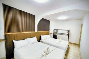 A hotel room with two beds, a wooden headboard, a bedside table, a lamp, and a small shelf. - 3-bedroom townhome in delightful Pattaya City with AC (Pattaya City)