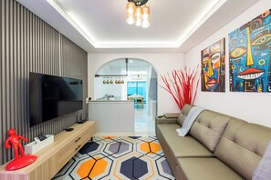 A modern living room with a flat-screen TV, a sofa, a patterned rug, and abstract wall art. - 3-bedroom townhome in delightful Pattaya City with AC (Pattaya City)