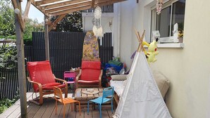 Une terrasse en bois avec une tente indienne blanche, des chaises rouges et bleues, et une table.