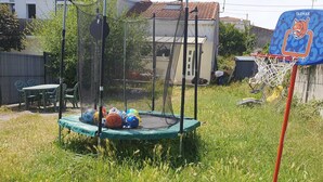 Un trampoline doté d’un filet de protection, entouré de pelouse et agrémenté d’un panier de basket.