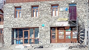Un edificio de dos pisos con fachada de piedra, balcón de madera y un letrero que indica una casa de huéspedes y mercado.