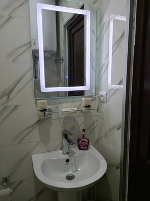 A bathroom with a white sink, a mirror with a light, and a shower visible in the background.