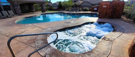 A swimming pool with a hot tub and a wooden structure in the background.