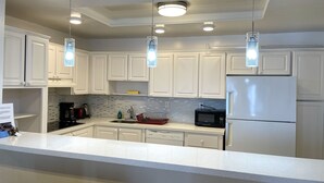 A modern kitchen with white cabinets, a stainless steel refrigerator, a microwave, and pendant lights. - Modern Sunny Isles Condo Near Beach (Sunny Isles Beach)
