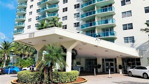 A modern multi-story hotel with a covered entrance, palm trees, and a parking area. - Modern Sunny Isles Condo Near Beach (Sunny Isles Beach)