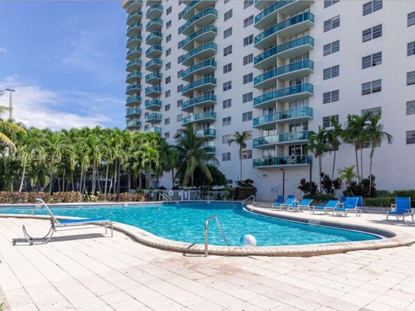 A hotel with a pool area, palm trees, and a multi-story building with balconies.