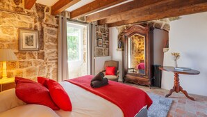 A bedroom with a stone wall, wooden beams, a bed with red pillows, a mirror, and a small table. - Character Stone House in the Heart of Medieval Montréal, Ardèche (Montréal)