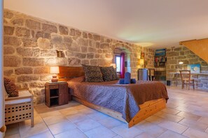 Ein Schlafzimmer mit Stehwand, einem Bett mit gemusterten Textilien, einem kleinen Nachttisch und einem Stuhl.