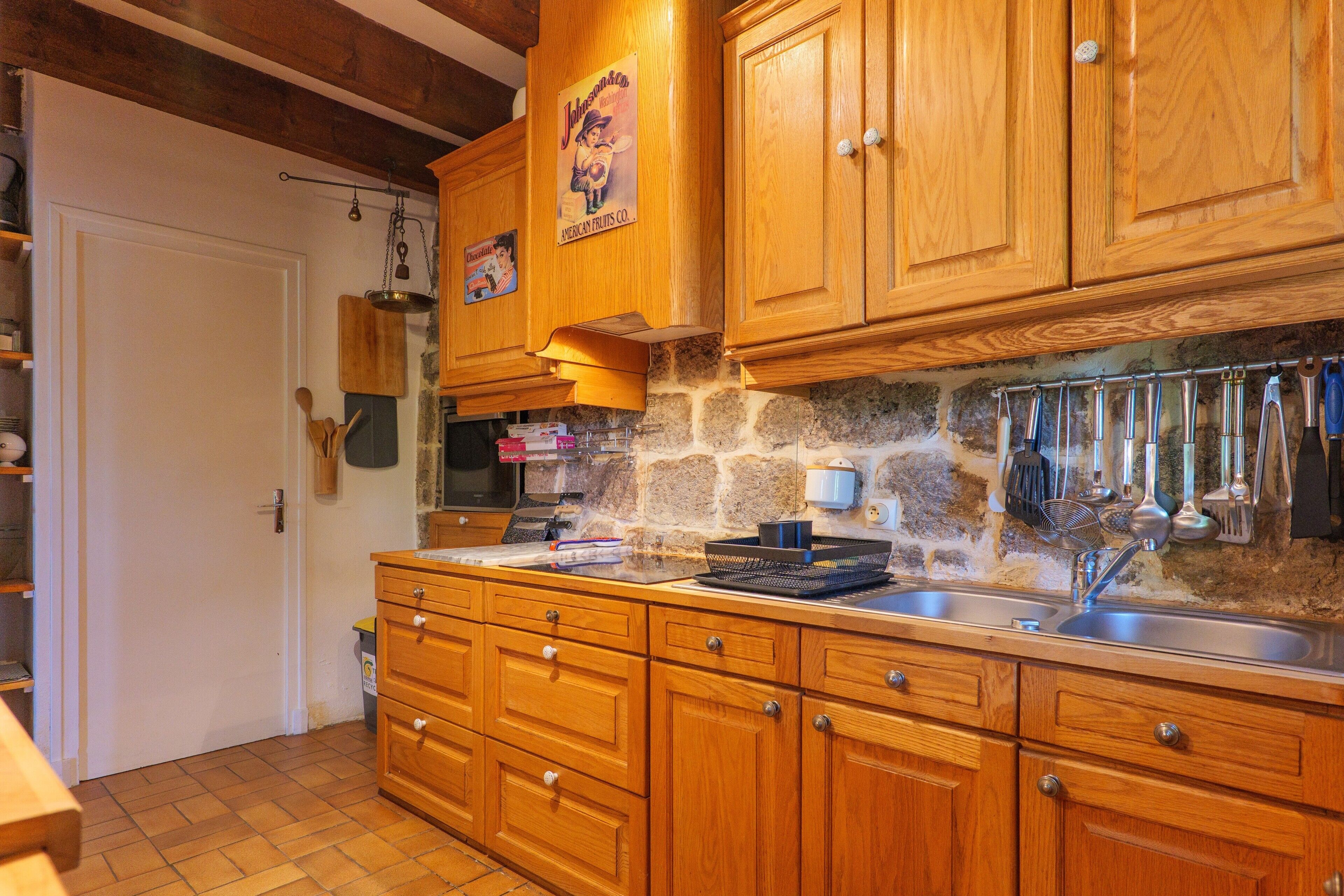 Una cocina con armarios de madera, salpicadero de piedra y diversos utensilios de cocina colgados en la pared.