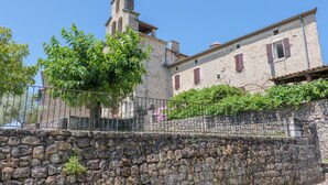 A stone building with a bell tower, a stone wall, and a metal fence. - Character Stone House in the Heart of Medieval Montréal, Ardèche (Montréal)