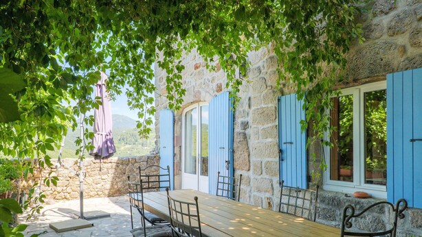 A stone patio with a wooden table and chairs, surrounded by blue shutters and a stone wall. - Character Stone House in the Heart of Medieval Montréal, Ardèche (Montréal)