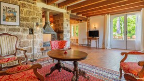 A stone-walled room with a round wooden table, two upholstered chairs, a fireplace, and a television. - Character Stone House in the Heart of Medieval Montréal, Ardèche (Montréal)