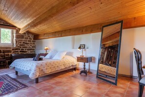 Un dormitorio con cama, mesita de noche, espejo, pared de piedra y ventana.