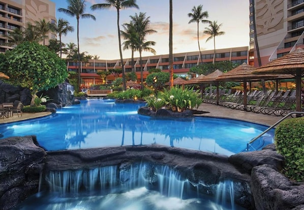 Ein Hotelpool mit Wasserfall, Palmen und Liegestühlen.