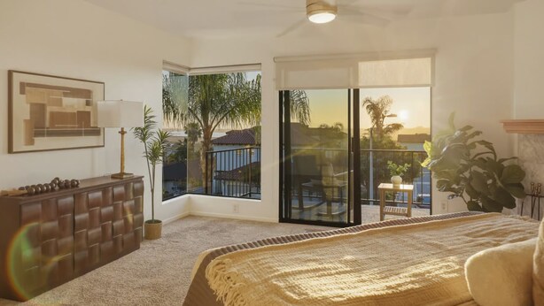 Ein Schlafzimmer mit großem Fenster, Deckenventilator, Bett und Blick auf einen Balkon.