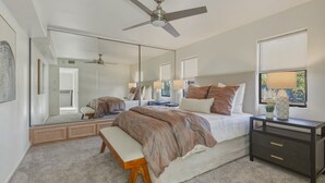 Ein Schlafzimmer mit einem großen Bett, einem Nachttisch, einer Bank, einem Deckenventilator und einem großen Spiegel.