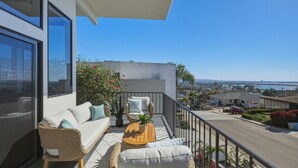 Ein Balkon mit einer Couch, Korbstühlen, einem kleinen Tisch und einem Blumentopf.
