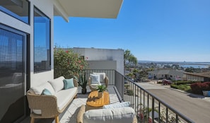 Ein Balkon mit einer Couch, Korbstühlen, einem kleinen Tisch und einem Blumentopf.