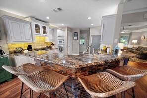 A kitchen with a central island, bar stools, and a dining area with a couch. - Isleview Retreat on Callendar Lake (Murchison)