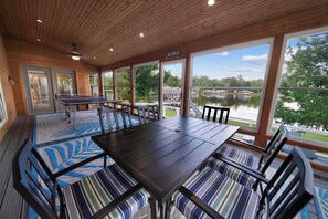 A covered outdoor dining area with a ping pong table, a large table, and chairs, overlooking a lake with a dock and boats. - Isleview Retreat on Callendar Lake (Murchison)