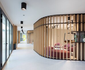 Un interior moderno con un separador de madera curvada, suelo blanco y una zona de estar con sillas rojas.