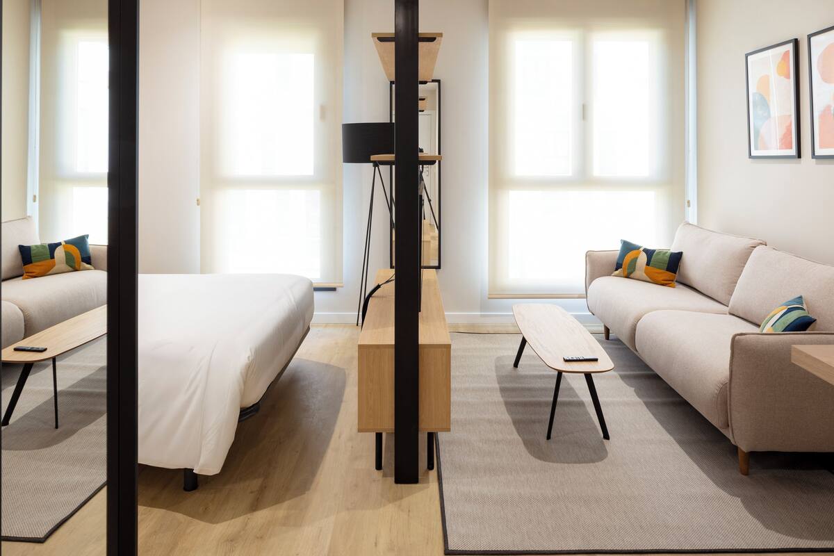 Una habitación de hotel moderna con cama, sofá, escritorio y un espejo grande.