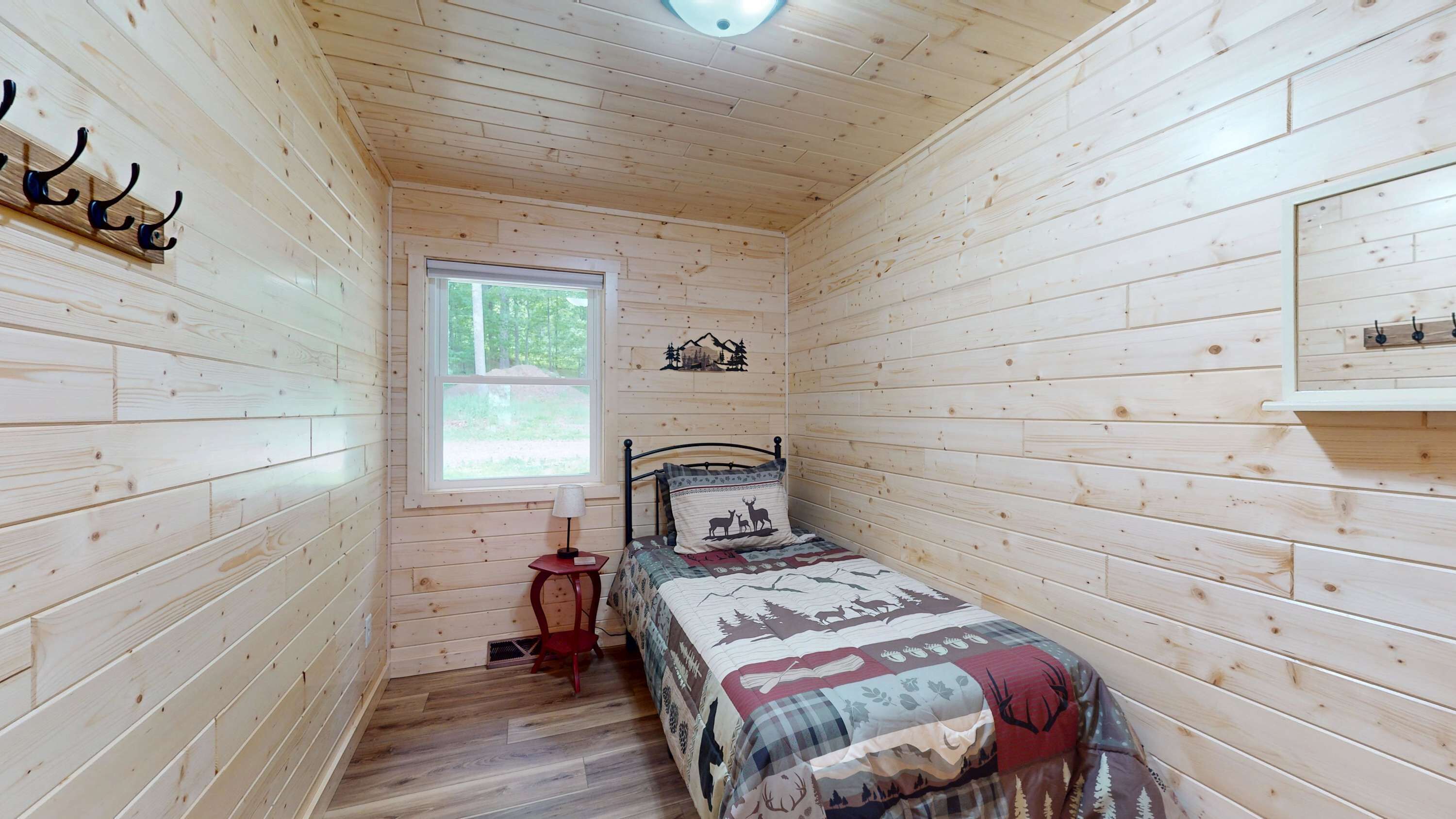 A small, wooden cabin bedroom with a bed, a nightstand, a lamp, a window, and a wall-mounted shelf.
