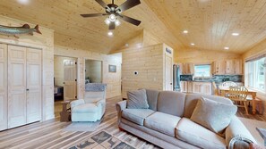 A wooden cabin interior with a sofa, armchair, dining table, and kitchen area. - American Eagle Retreat (Conover)