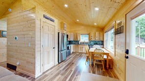 A wooden cabin interior with a kitchen, dining area, and a large window. - American Eagle Retreat (Conover)