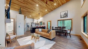 A spacious living area with a wooden ceiling, a kitchen, and a dining area with a view of the outdoors.