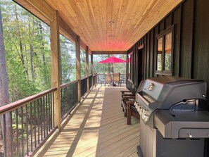 Una terraza techada con una parrilla, barandas de madera y vista a un bosque.