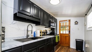 A kitchen with black cabinets, a marble countertop, a stainless steel sink, and a microwave. - The Cozy Corner House (Kissimmee)
