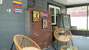 A covered outdoor area with two wicker chairs and a glass table. - The Cozy Corner House (Kissimmee)