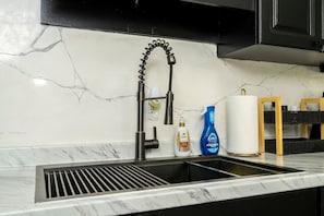 Una cocina con un grifo negro, encimera de mármol y un lavabo. Hay dos botellas de jabón Dove y un limpiador Dawn Power and Performance sobre la encimera.