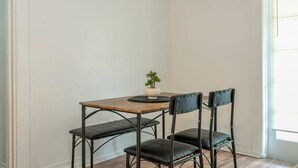 A corner room with a wooden table, two black chairs, a small potted plant, and a window with blinds. - The Cozy Corner House (Kissimmee)