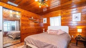 A wooden-paneled bedroom with a bed, bedside lamps, and a mirror. - The Cozy Corner House (Kissimmee)