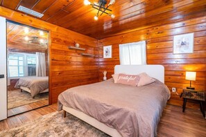 Ein Schlafzimmer mit Holzwänden, einem Bett, Nachttischlampen und einem Spiegel.