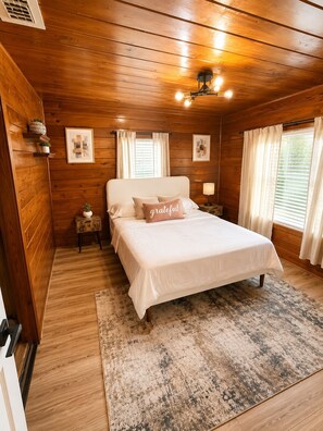Camera da letto con rivestimenti in legno, un letto, comodini, un tappeto e luci a soffitto.