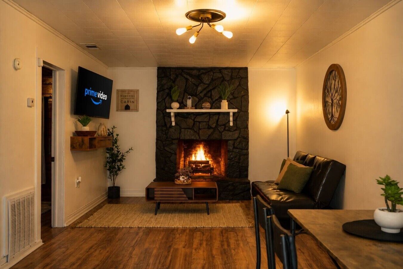 A cozy living room with a stone fireplace, a leather sofa, a flat-screen TV, and a dining area.